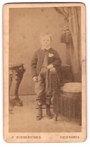 Fotografie P. Doebereiner, Caledonia /Ontario, Junge im Anzug neben Vorhang