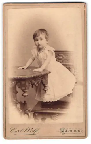 Fotografie Carl Wolf, Harburg, Kind auf kunstvollem Tisch