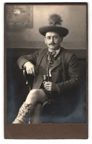 Fotografie H. Gutjahr, Ramsau, bayerischer Herr in Tracht mit Federhut und Lederhose, Pfeife rauchend auf einem Stuhl