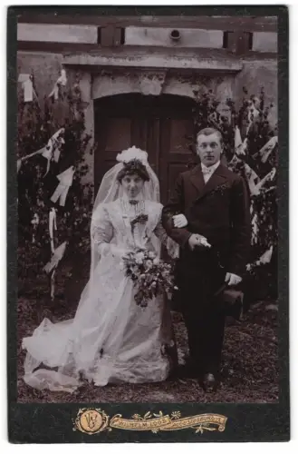 Fotografie Wilhelm Loos, Augustusburg i. E., Hochzeitspaar vor dekorativem Hintergrund