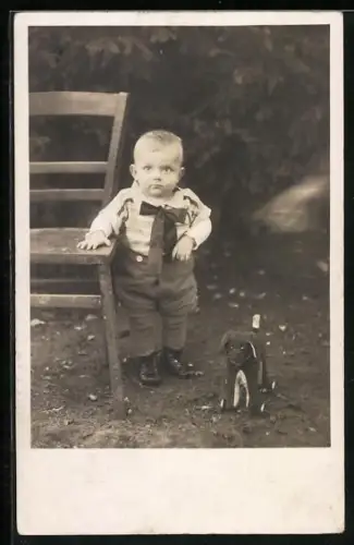 AK Knabe stehend neben Stuhl mit Spielzeughund