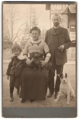 Fotografie unbekannter Fotograf und Ort, Familienportrait mit Dackel auf dem Schoss und Terrier an der Leine