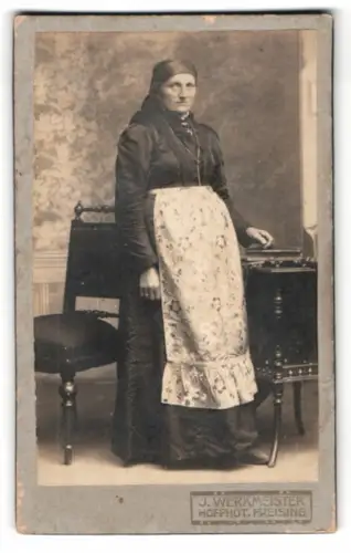 Fotografie J. Werkmeister, Freising, Stehende Frau mit Schürze neben Tisch und Stuhl, Tracht