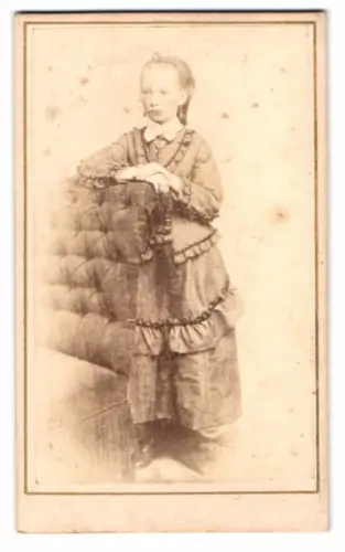 Fotografie unbekannter Fotograf und Ort, Mädchen im Kleid an gepolstertem Sessel