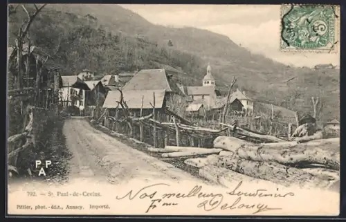 AK St. Paul-de-Cevins, Vue du village avec route bordée de clôtures en bois et église en arrière-plan