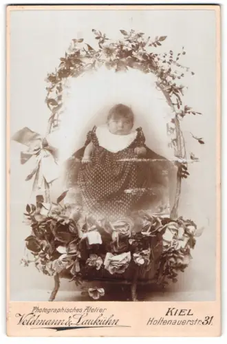 Fotografie Veldmann & Laubkühn, Kiel, niedliches Mädchen im Pünktchenkleid sitzt im Blumenkorb, Schnappschuss