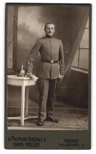 Fotografie Hans Möller, München, Soldat in Uniform nebst Pickelhaube auf dem Tisch