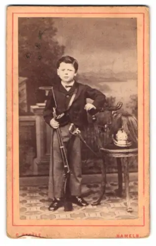 Fotografie C. Degèle, Hameln, Emmernstrasse 11, Junge mit Gewehr und Pickelhaube Rosshaarbusch