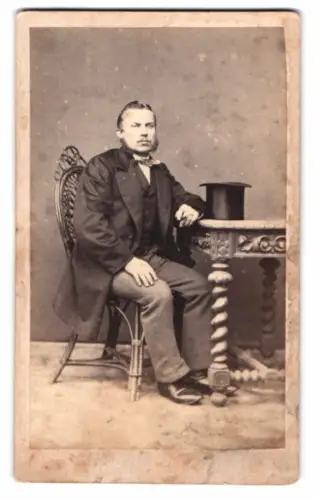 Fotografie P. Wacker, Bitterfeld, sitzender Herr mit Zylinder auf Tisch