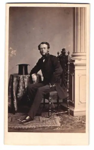 Fotografie A. Siegmund, Hamburg, Mann auf elegantem Stuhl neben Tisch mit Zylinder
