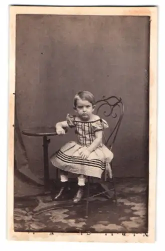 Fotografie unbekannter Fotograf und Ort, Kind auf einem Stuhl neben einem Tisch mit grimmigem Blick