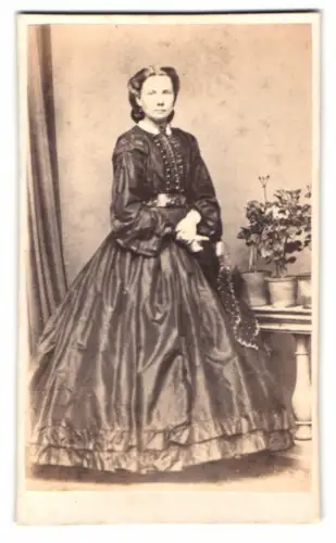 Fotografie unbekannter Fotograf und Ort, Frau in elegantem Kleid mit Pflanzenarrangement