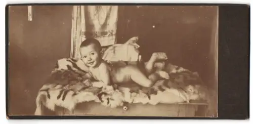 Fotografie unbekannter Fotograf und Ort, Baby auf Fell liegend 1914