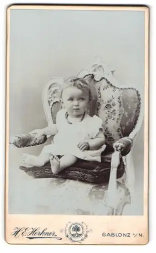 Fotografie Heinrich E. Herkner, Gablonz, Gebirgsgasse 22, Porträt eines Kleinkindes auf einem eleganten Stuhl