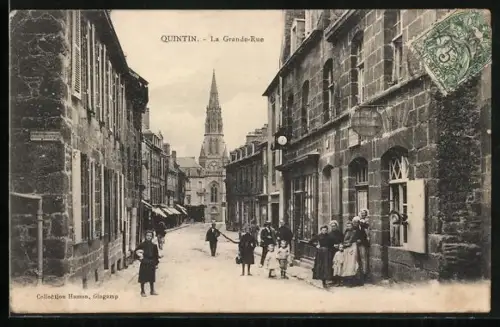 AK Quintin, La Grande-Rue avec des passants et vue sur l`église en arrière-plan