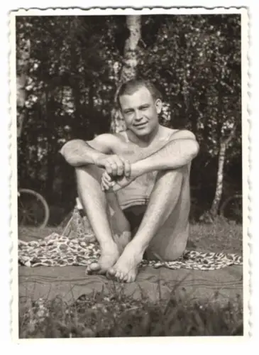 Fotografie junger Mann in Badehose auf einem Handtuch im Wald