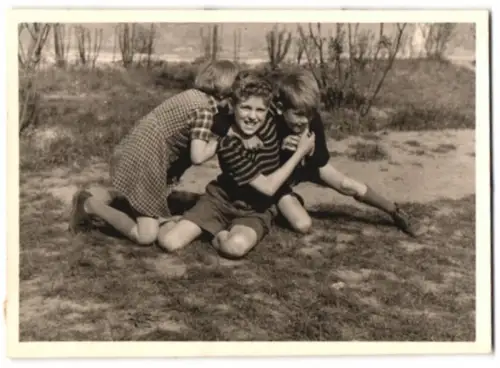 Fotografie zwei Jungen und ein Mädchen beim balgen auf einer Wiese