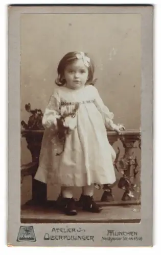 Fotografie Atelier Oberpollinger, München, Neuhauser Str. 44/45/46, Kleinkind mit Blume vor einer Ballustrade 1905