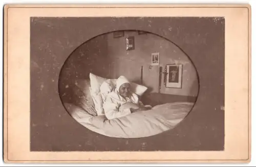 Fotografie unbekannter Fotograf und Ort, Ältere Dame / Grossmutter im Bett liegend mit Rosenkränzen an der Wand