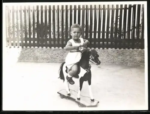 Fotografie kleines Kind auf seinem Schaukelpferd auf Rollen
