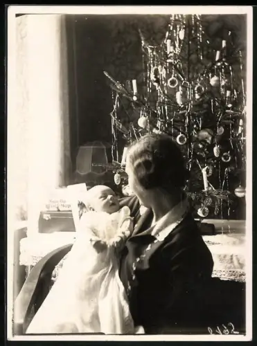 Fotografie junge Mutter hält an Weinachten ihr Kind im Arm, Weihnachtsbaum mit Lametta, Mutterglück
