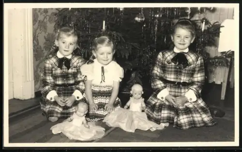 Fotografie drei junge Mädchen mit ihren Puppen zu Weihnachten vor dem Weihnachtsbaum