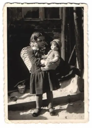 Fotografie niedliches Mädchen mit ihrer Puppe im Arm und Korb auf dem Rücken