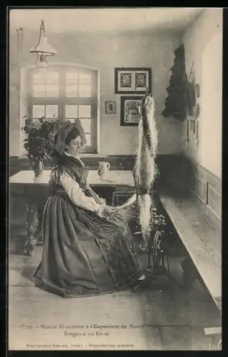 AK Nancy, Exposition, Maison Alsacienne, songeuse au rouet, Frau in Tracht sitzt am Spinnrad