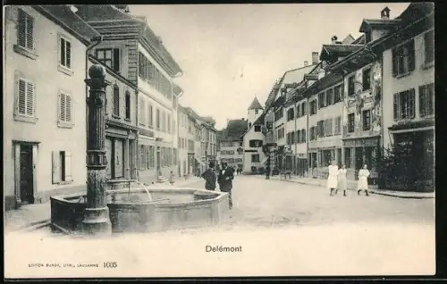 AK Delemont, Strassenpartie mit Brunnen und Geschäften