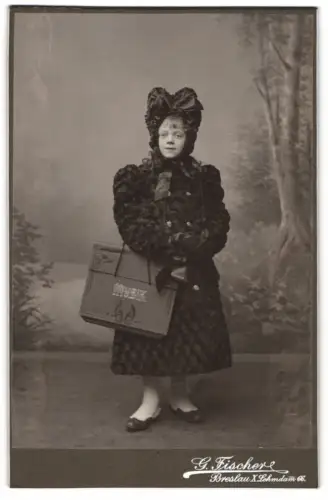 Fotografie G. Fischer, Breslau, junges Mädchen im schicken Winterkleid mit Haube und Musik Tasche