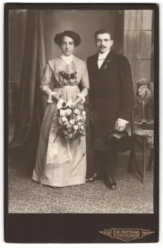 Fotografie E.W. Matthias, Seifhennersdorf, Stehend vor Vorhang, elegantes Brautpaar mit Blumenstrauss