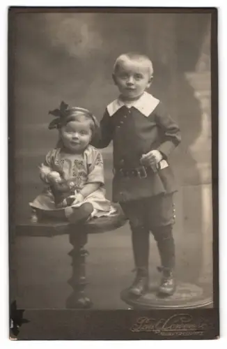 Fotografie Paul Löwenhag, Marktredwitz, Zwei Kinder auf Tisch und Hocker mit Puppe im Arm