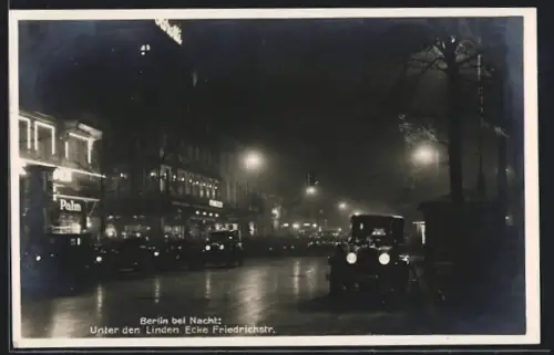 AK Berlin, Unter den Linden Ecke Friedrichstr., Nachtansicht mit Autos und beleuchteten Gebäuden