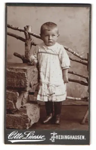 Fotografie Otto Luesse, Thedinghausen, Junge in weissem Kleid vor rustikalem Zaun