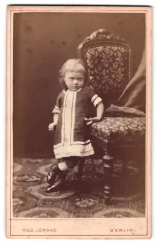 Fotografie Rud. Conrad, Berlin, Alexanderstrasse 44, Kleinkind mit gepolstertem Stuhl