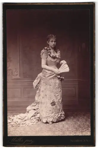 Fotografie Müller jun., Wien, hübsche junge Frau Lena im verzierten Kleid mit Fächer und Kruzifix Halskette