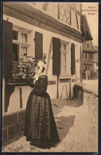 AK Schleithal /Alsace, Alsacienne en costume traditionnel devant une maison à colombages
