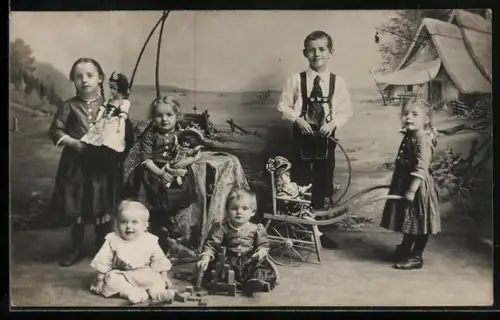 Foto-AK Kindergruppe mit Puppen u. Schubkarre vor Fotokulisse