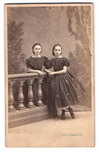 Fotografie L. Haase & Co., Berlin, zwei niedliche junge Mädchen posieren an einem Geländer vor einer Studiokulisse