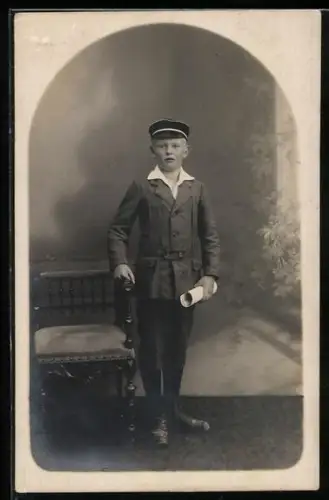 Foto-AK Junge mit Schirmmütze am Stuhl in einer Studiokulisse