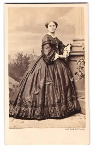 Fotografie Carl Suck, Berlin, Portrait Dame im glänzenden Biedermeierkleid vor einer Studiokulisse