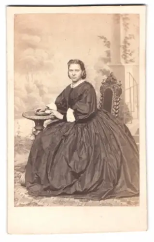 Fotografie Portrait junge Frau im weiten dunklen Kleid sitzend vor einer Studiokulisse