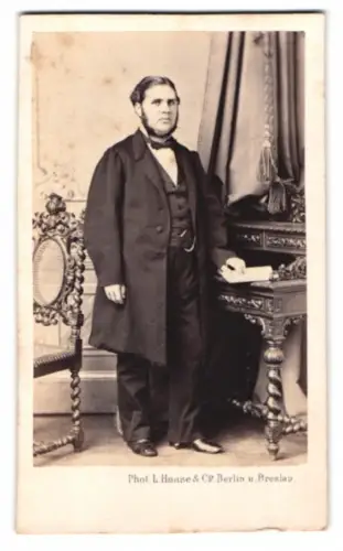 Fotografie L. Haase & Comp., Berlin, Friedrichstrasse 178, Herr im Anzug neben Tisch stehend