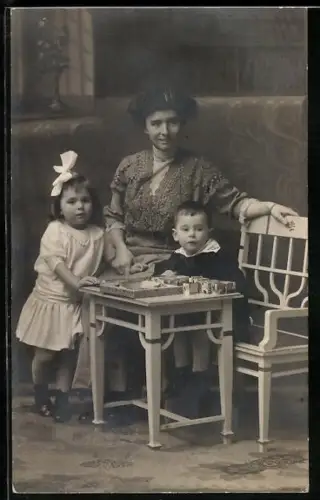 Foto-AK Mutter mit ihren zwei Kinder an einem Tisch 1915, Bauklötze auf dem Tisch