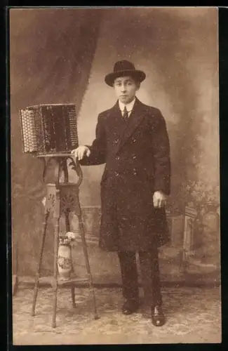 Foto-AK Mann im Mantel steht neben einem Akkordeon
