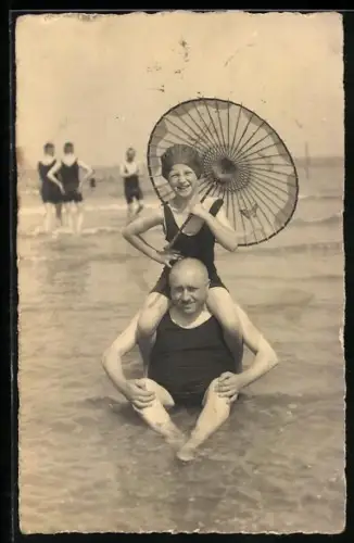 AK Mann im flachen Wasser sitzend, Mädchen im Badeanzug mit Sonnenschirm