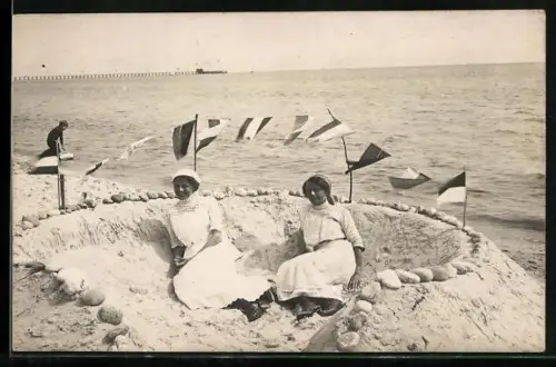AK Zwei Frauen in Strandkleidung liegen in einer Sandburg am Ufer