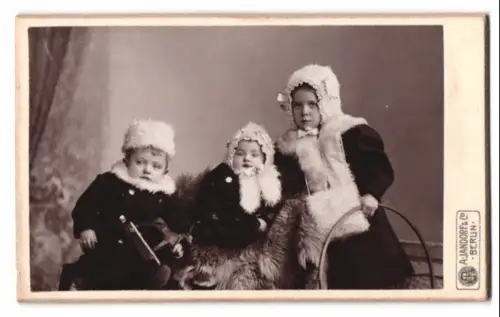 Fotografie A. Jandorf & Co., Berlin, drei kleine Kinder in Winterkleidung mit Spielzeug in der Hand
