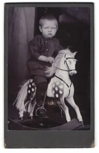 Fotografie junger Knabe reitet auf seinem Schaukelpferd