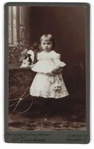 Fotografie W. Jacobsen, Kiel, niedliches Mädchen im weissen Kleid mit Puppenwagen und Puppe
